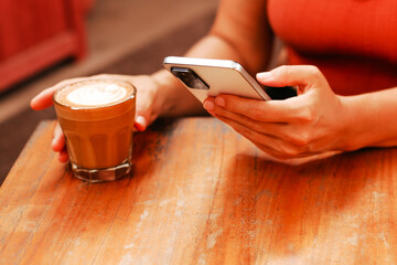 Female hands holding smartphone and glass with cappuccino. The blogger makes posts and uploads photos on social networks. On-line training and work