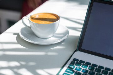 Hot black coffee and laptop on white table. Concept of working on a tablet in a cafe in the morning. Freelancer's workplace.