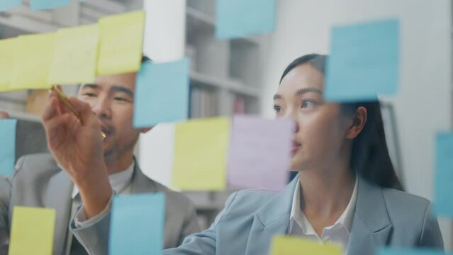 Close up of hands write business strategy on paper sticky notes and paste on the board for business planning and marketing.