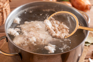 Metal skimmer and meat broth foam. Dirty kitchen utensils in a metal bowl. Cooking a family dinner. Selective focus.
