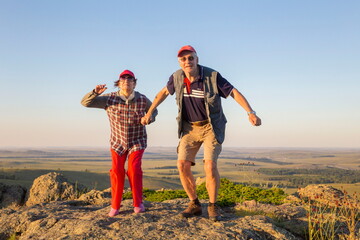 a beautiful mature couple on a high rock admires the Ural nature and the Ai river on a summer sunny day