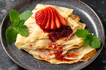 Delicious thin pancakes or crepes with strawberries and jam