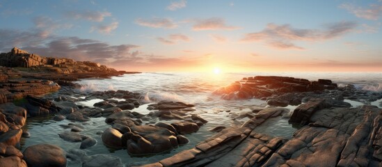 The sun is setting over a rocky beach, casting a warm glow over the rugged terrain and calm waters. The scene captures the beauty of nature as day transitions to night.