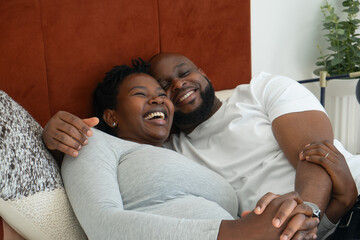 Smiling man embracing pregnant woman on bed