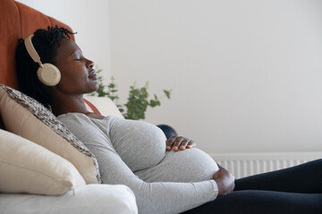 Pregnant woman with headphones relaxing on bed