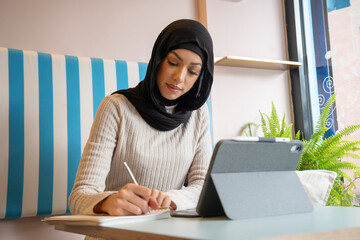 Young woman in hijab working on tablet in cafe