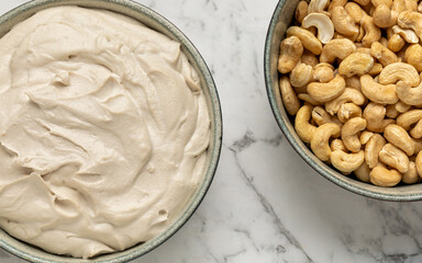 Top view of homemade vegan cultured cream cheese made from cashew nuts in a bowl, cashew huts in the second. Alternative dairy-free diet, plant-based food.