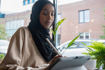 Young woman in hijab working on tablet in cafe