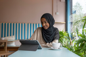 Young woman in hijab working on tablet in cafe