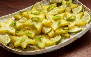 Homemade carambola or star fruit spicy salad with green chili, lime pieces, and lime juice. Perfect condiment for grilled fish or a curry. Wooden table.