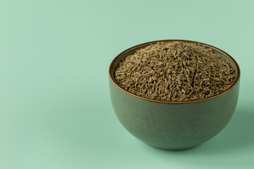 Whole cumin seeds in a bowl. An empty blue-green background with space for text.