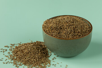 Whole cumin seeds in a bowl. A heap of seeds on the table near the bowl. 