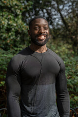 Portrait of smiling athletic man with earbuds standing in park