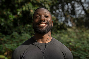 Portrait of smiling athletic man with earbuds standing in park