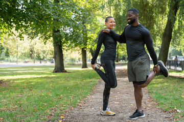 Smiling man and woman stretching legs in park - obrazy, fototapety, plakaty