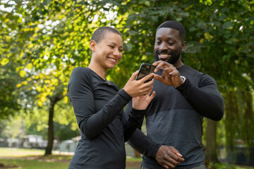 Smiling athletic man and woman looking at smart phone in park