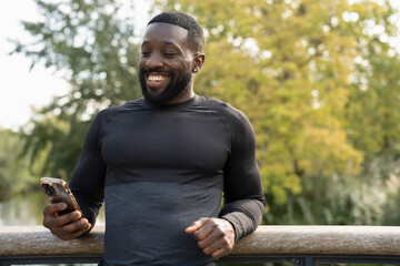 Smiling athletic man looking at smart phone on footbridge in park