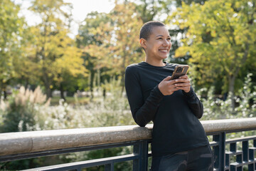 Smiling athletic woman with smart phone on footbridge