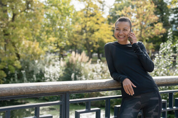 Fototapeta premium Smiling athletic woman with smart phone on footbridge