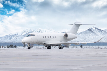 White luxury executive airplane taxiing on airport taxiway in winter on the background of high...