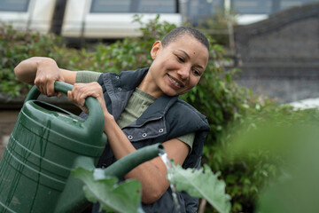 Smiling woman watering homegrown vegetables in urban garden