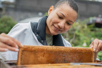 Smiling female beekeeper removing frame from beehive in urban garden