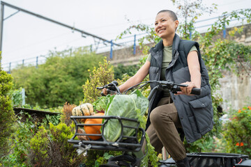 Smiling woman riding cargo electric trike loaded with homegrown vegetables