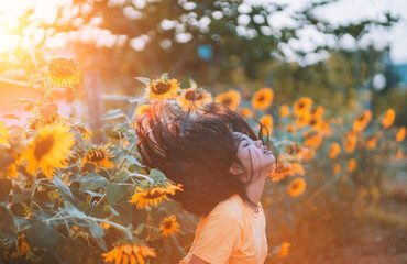 A young woman sits and shakes her hair against a sunflower plant.
