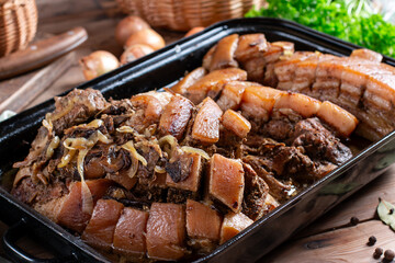 Fresh cooked roasted pork on a baking tray served on a wooden table, typical Czech food