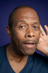 Portrait of man with hand on ear against purple background