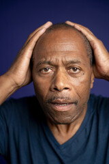 Portrait of worried man with hands on head against purple background