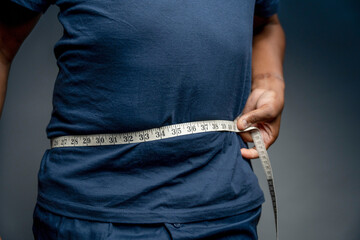 Senior man measuring waist against gray background