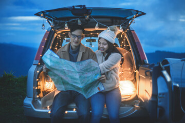 Smiling couple sitting and reading a map in the back of a car with camping lights