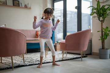 Little girl dancing with headphones in living room - obrazy, fototapety, plakaty