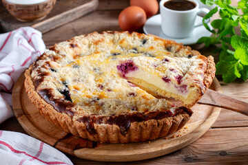 Homemade raspberry pie with short pastry, ripe raspberries and blueberries cut into pieces on a wooden table.