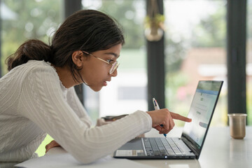 Girl doing homework and using laptop in living room