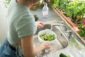 Young woman washing food in kitchen sink - obrazy, fototapety, plakaty