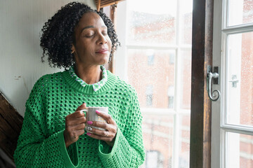 Thoughtful woman holding cup of coffee by window