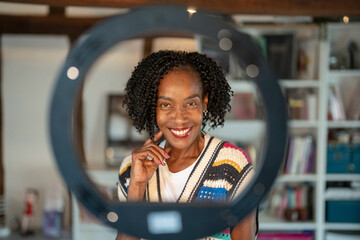 Portrait of smiling woman standing in front of ring light at home