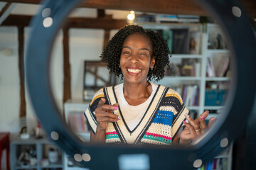 Smiling woman standing in front of ring light at home - obrazy, fototapety, plakaty