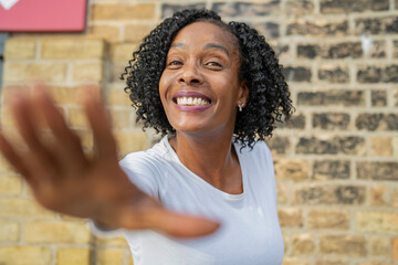 Portrait of smiling woman with hand raised against brick wall