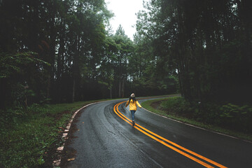 Obraz premium Woman in yellow raincoat running on road in pine forest