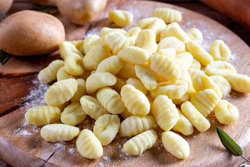 Fresh homemade uncooked gnocchi Italian dumplings on a floured wooden board in a kitchen with fresh greens behind in a close up