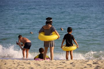 Family with children on a sea beach. Mother with sons wearing inflatable rings going to swim