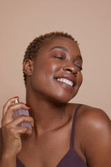 Studio portrait of smiling woman spraying perfume on neck