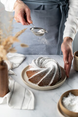 Woman's hands sprinkling icing sugar over cake. Powder sugar falls on cake.