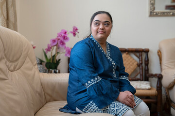 Portrait of young woman with down syndrome sitting on sofa at home