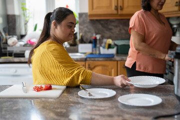 Woman with down syndrome preparing tableware while cooking with mother