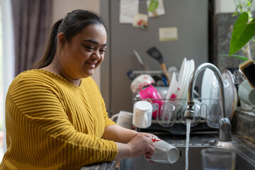 Young woman with down syndrome washing dishes at home - obrazy, fototapety, plakaty
