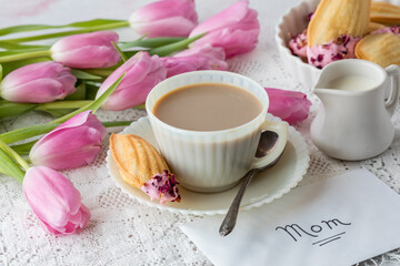 Fototapeta na wymiar A Mother's Day concept with a cup of tea, French Madeleine's and pink tulips.